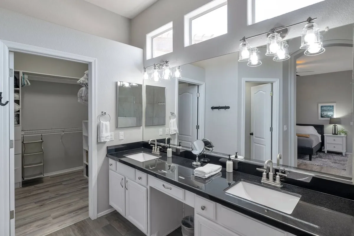 A modern bathroom featuring dual sinks with large mirrors, an open closet, and sleek light fixtures. The space is fresh, organized, and perfect for morning routines or quiet moments of self-care.