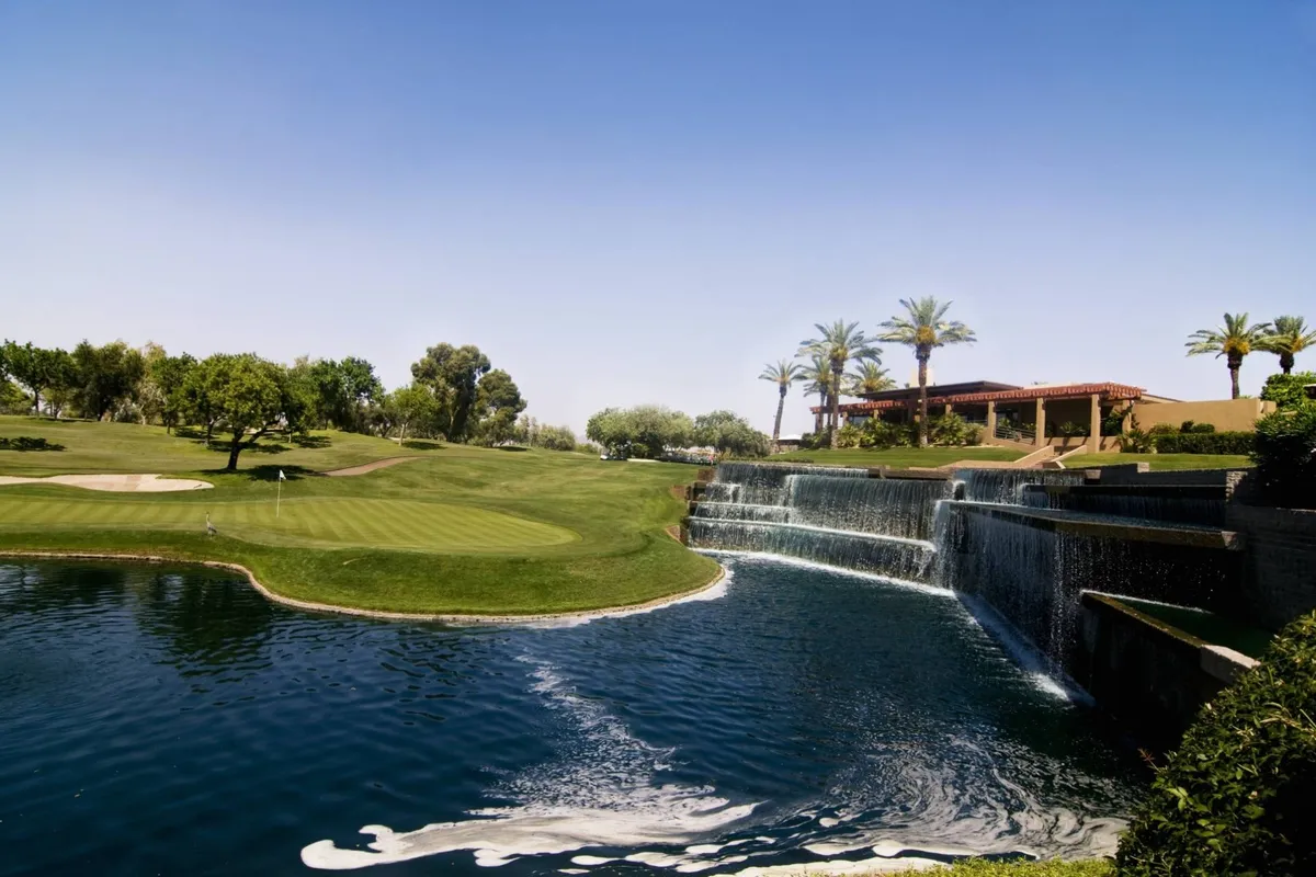 A scenic view of a nearby golf course with a waterfall, swimming pool, palm trees, and a clubhouse, capturing opportunities for socializing, recreation, and relaxation.