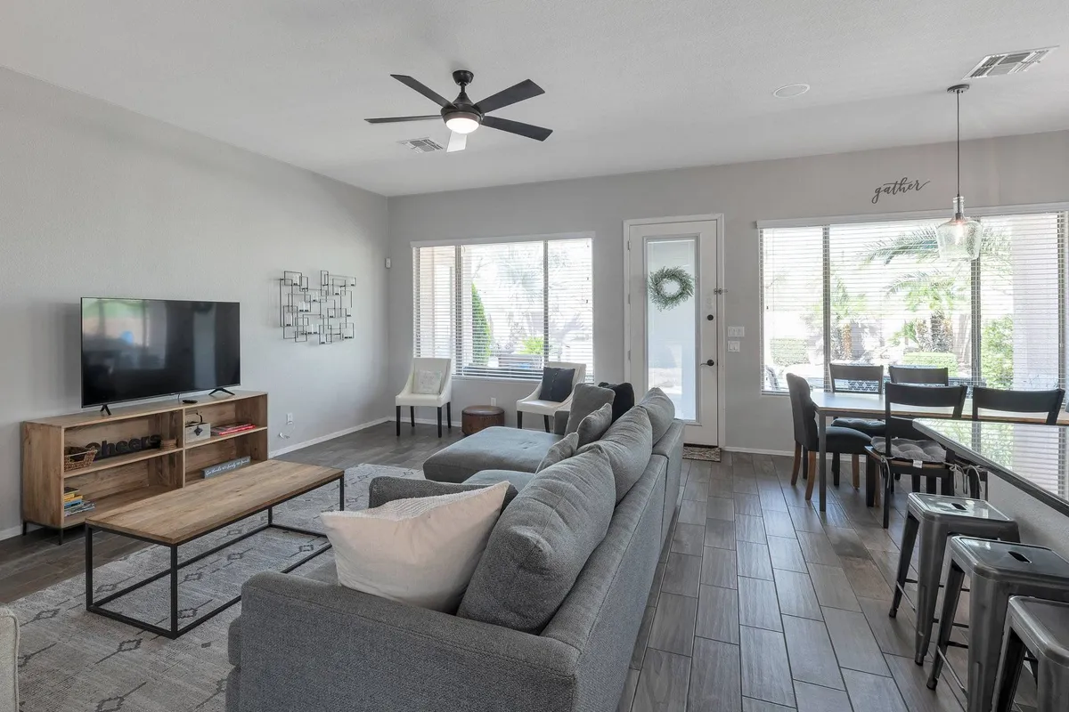A welcoming open-plan interior where the dining table for six anchors the room, with adjacent living and dining spaces. Large windows provide natural light, and the setup encourages gathering and conversation.
