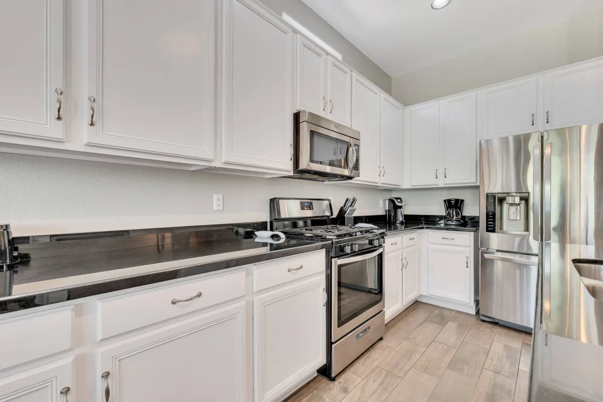 A contemporary kitchen setting featuring stainless steel appliances, black granite countertops, and white cabinetry. The design is both functional and stylish, hinting at a well-equipped space ideal for cooking and entertaining.