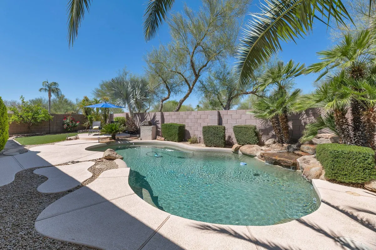 A beautifully landscaped backyard with a heated swimming pool, framed by lush palm trees and gardens. The scene includes ample space for swimming, sunbathing, and outdoor dining, with the lighting suggesting either morning or sunset ambiance.