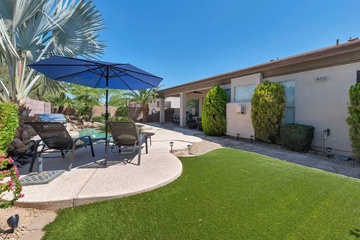 This image captures an inviting outdoor area featuring a blue umbrella, lawn chairs, artificial grass, and palm trees. The scene encourages relaxation and outdoor enjoyment, ideal for families looking to lounge or play together in the sun.